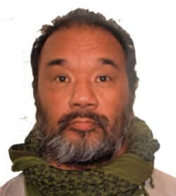 A photo of Marcel Marania, Grants Manager, a middle-aged, swarthy, Filipino man with salt and pepper moustache and beard and short dark hair wearing a olive brown scarf and a tan shirt.