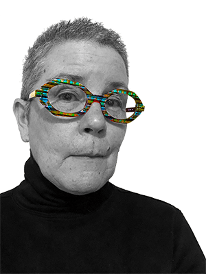 Suki OKane, a light-skinned older woman looking slightly skeptical with short, curly, grey hair and colorful plaid eyeglasses wearing a black turtleneck