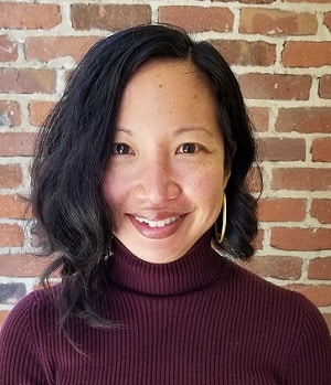 Pui Ling Tam, Program Lead, Economic Well-Being, a picture of a women with medium length dark hair wearing a maroon turtleneck in front of a brick wall