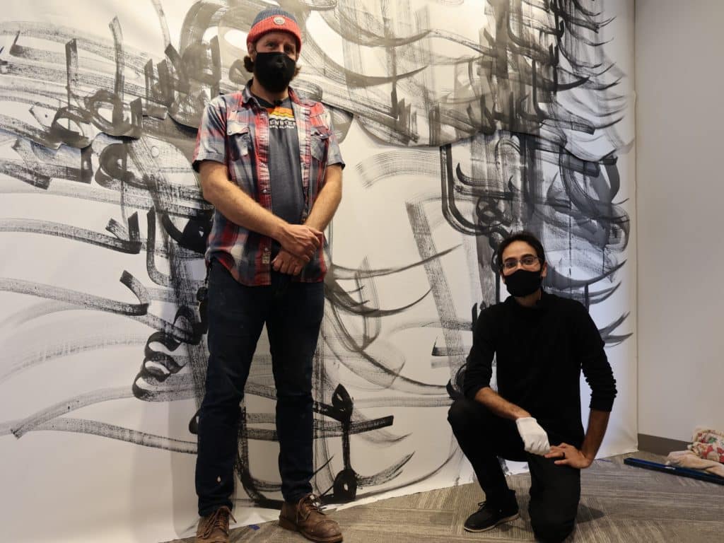 The two artist pose in front of a calligraphed curtain.