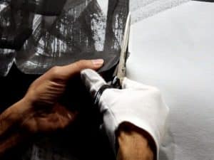Close up of two hands cutting a canvas with calligraphy on it.