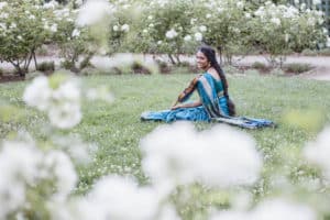 Artist Sruti Sarathy sits outside on the grass, playing a violin.