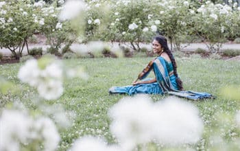 Artist Sruti Sarathy sits outside, wearing a blue sari and playing a violin
