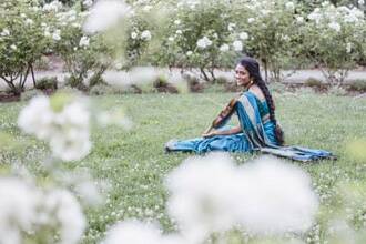 Artist Sruti Sarathy sits outside, wearing a blue sari and playing a violin