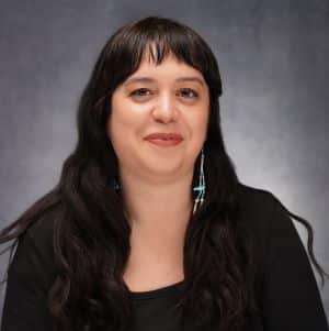 A women with long dark hair and turquoise beaded earrings wearing a black jacket and shirt