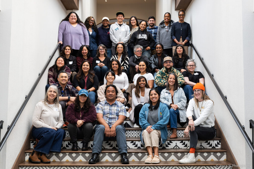 a diverse group of people smiling while sitting and standing on a staircase