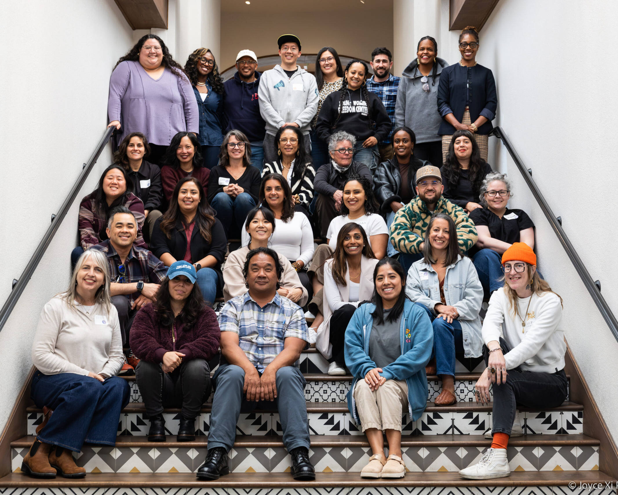 a diverse group of people smiling while sitting and standing on a staircase